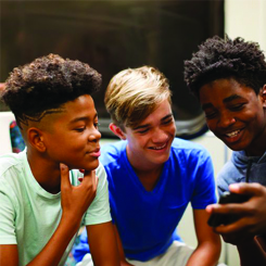 A group of boys checking a phone while smiling.