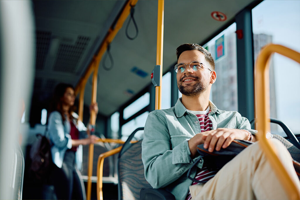 A male bus patron, happily smiling while looking out the window of a bus.