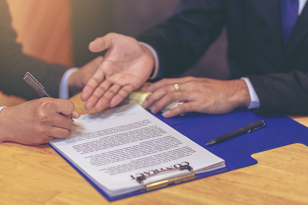 People reviewing and signing a document on a desk.