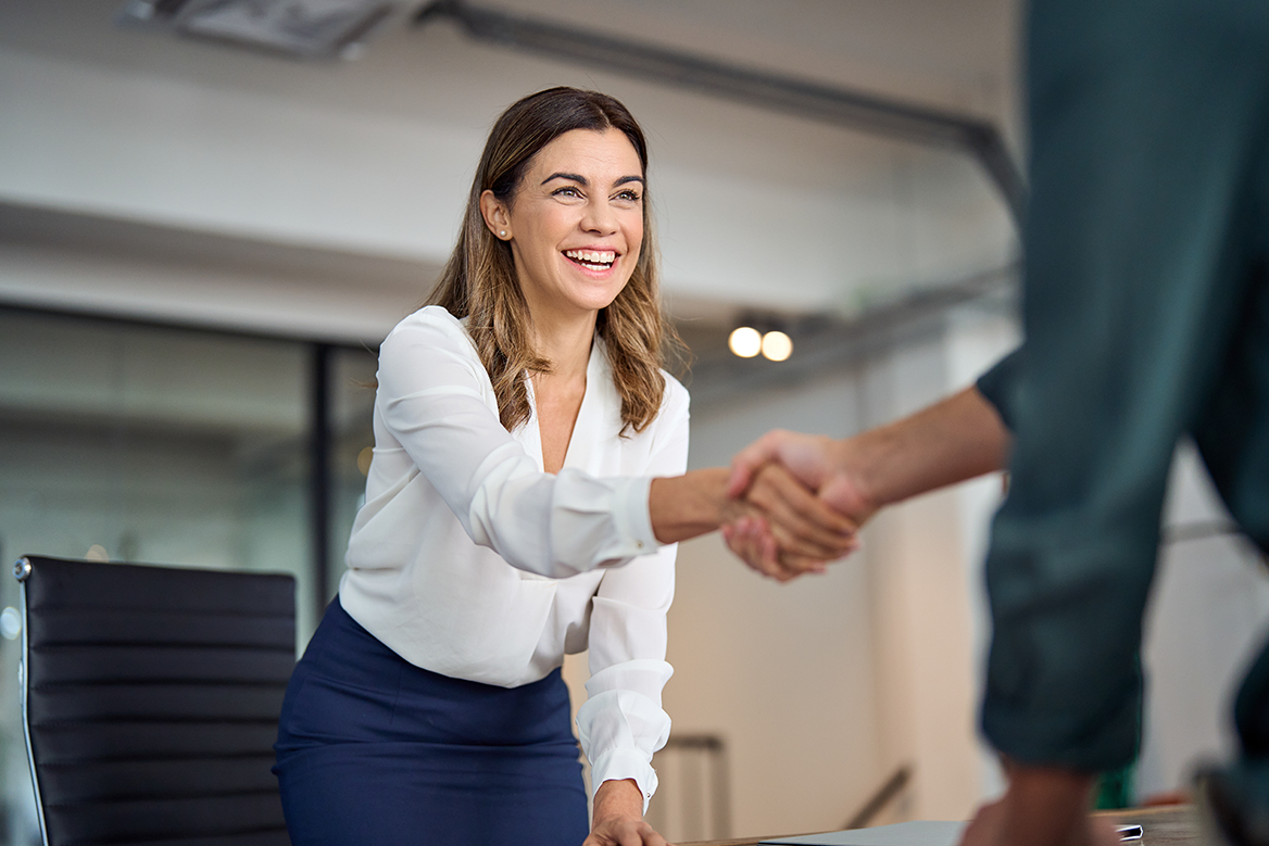 A female business associate shaking hands with someone across an office desk.