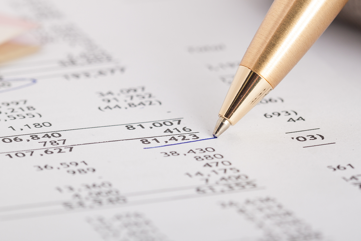 Up close perspective of a financial report and a pen underlining a number.