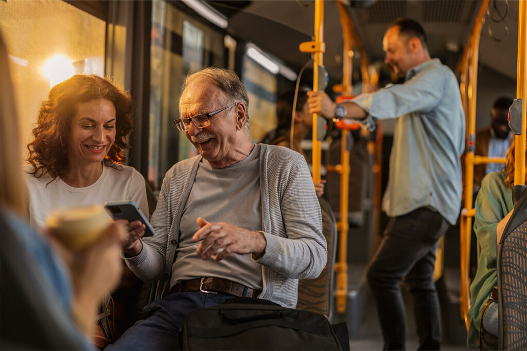 Bus patrons enjoying the ride while smiling at a cell phone.
