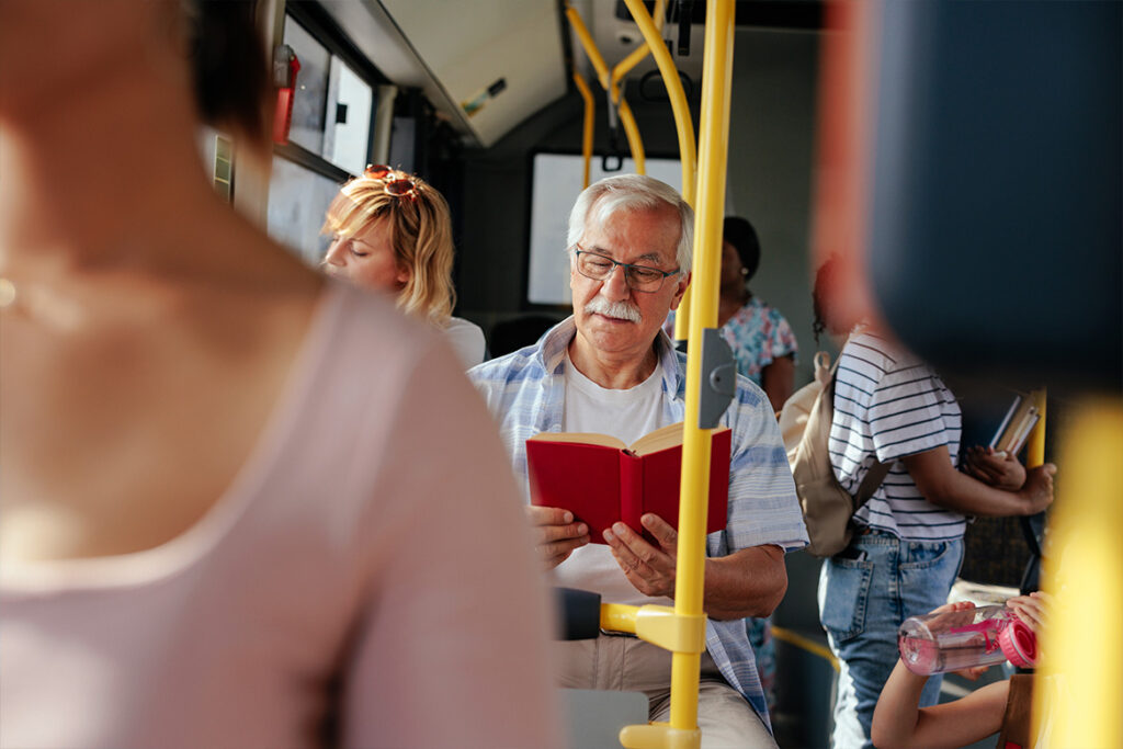 An elderly patron reading a book while enjoying his bus ride.