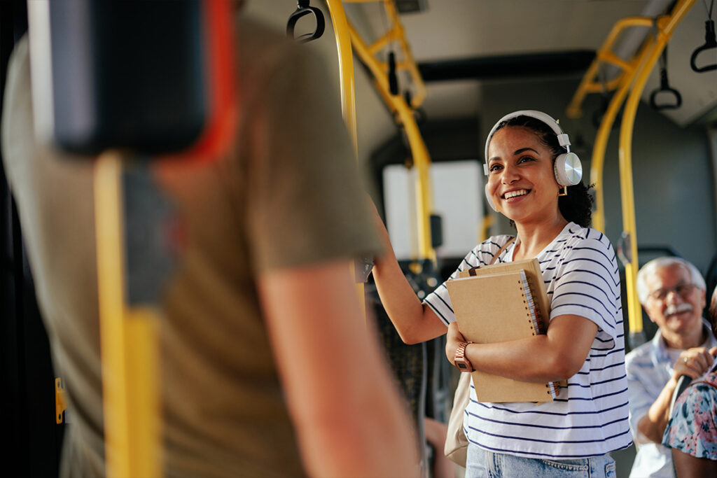 Student on bus smiling while holding notepads and books.