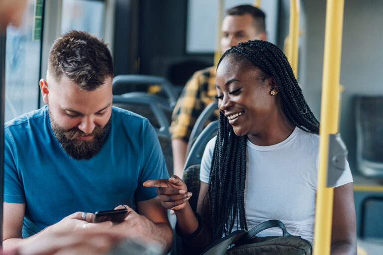Bus patrons having a conversation and reacting to something on a cell phone.