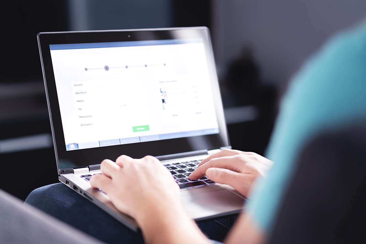 A from behind view of a person using a laptop to fill out an online form.